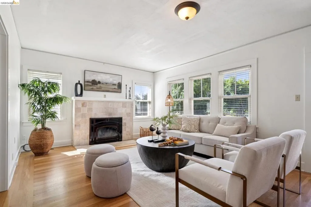 Living area featuring wood-finish flooring, a tiled fireplace with a dark insert, a central ceiling light fixture, and multiple windows with blinds
