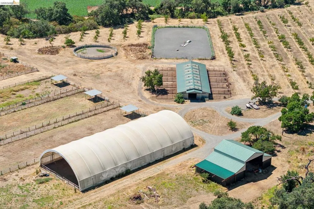 Expansive agricultural property featuring multiple structures, including a large arched fabric building, a barn with a green metal roof, and an additional building with a green metal roof