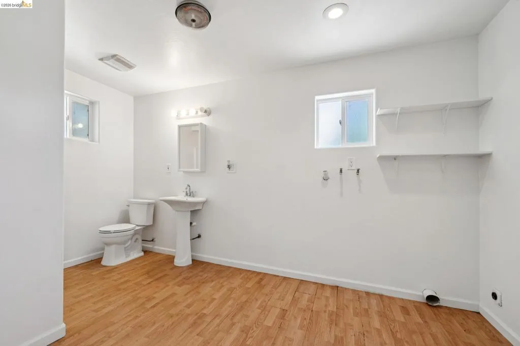 Spacious room featuring wood-finish flooring, a toilet, and a pedestal sink with a medicine cabinet