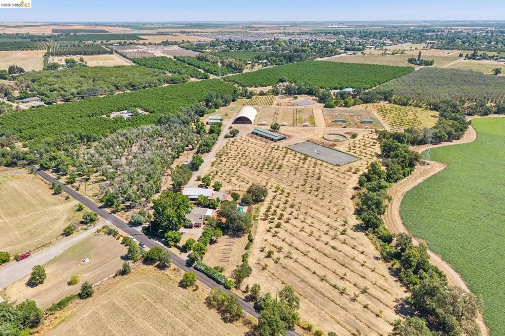 Expansive agricultural property featuring multiple cultivated fields, an equestrian arena, and a large quonset hut structure