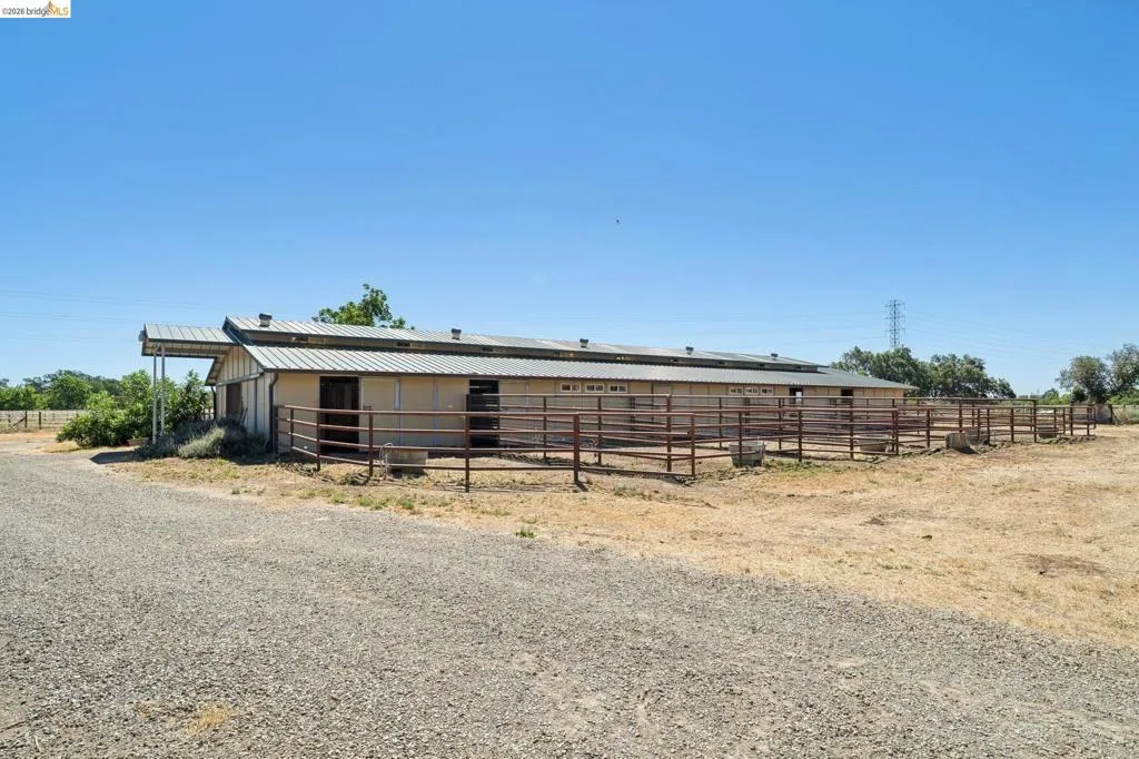 Agricultural structure with corrugated metal roofing, multiple stalls, attached covered overhang, and extensive metal paddock fencing