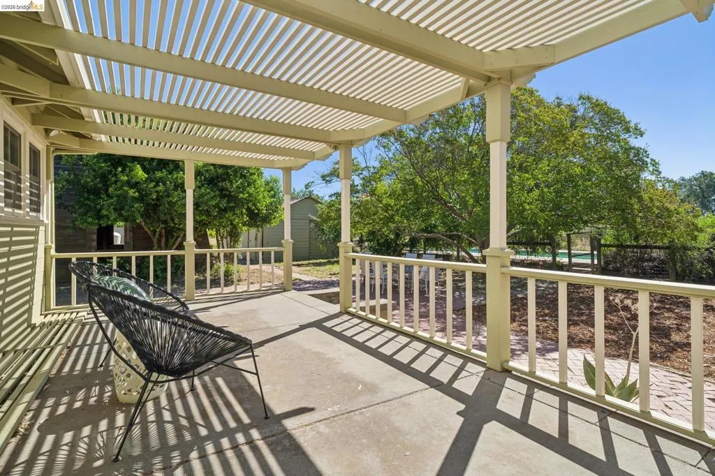 Covered patio featuring a slatted pergola, painted wood columns, and a railing