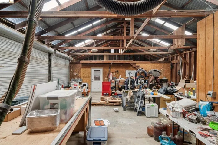 Spacious workshop featuring exposed wood beam ceiling, corrugated metal roofing, multiple skylights, concrete flooring, and an overhead garage door