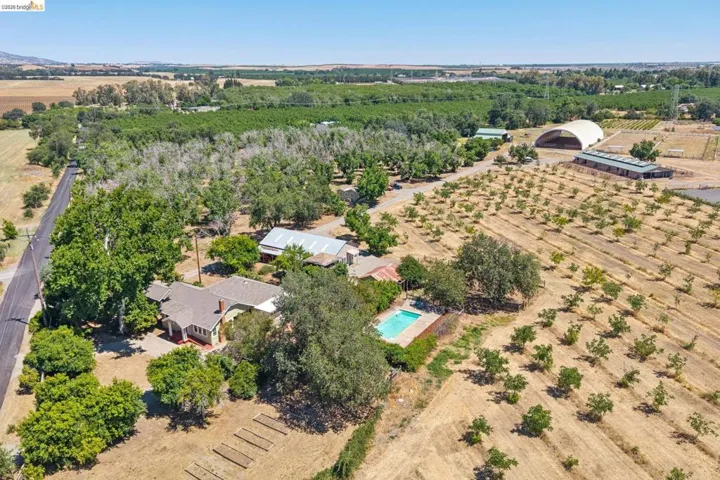 Sprawling acreage featuring a main residence, an outdoor swimming pool, extensive orchards, an agricultural building, and a large quonset hut