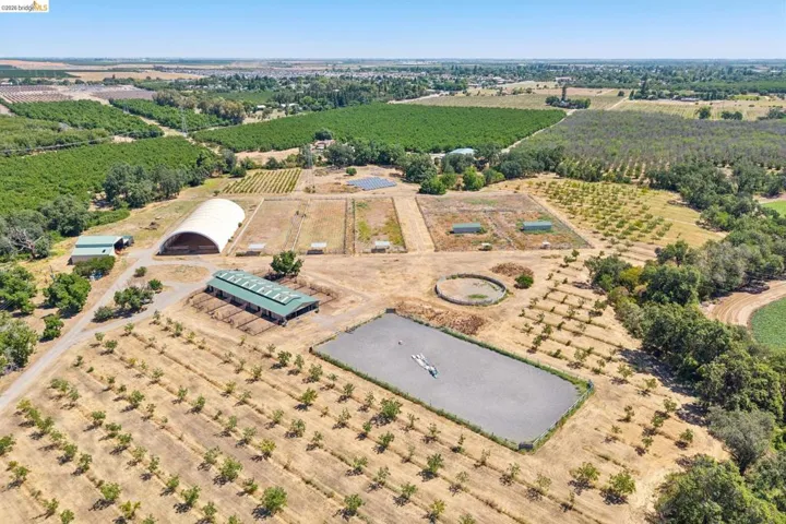Expansive agricultural property featuring multiple cultivated fields, an outdoor riding arena, a large covered structure, and additional outbuildings