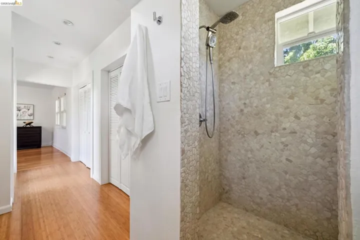 Walk-in shower with pebble tile surround and flooring, featuring a window and shower head with handheld attachment