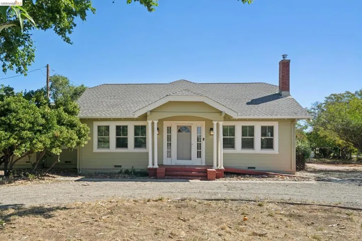 Ranch-style residence featuring a prominent front porch with columns, a light green exterior, and a red brick chimney