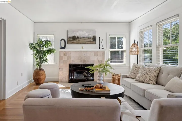 Living area featuring wood-finish flooring, a tiled fireplace with a black insert, white walls, and multiple windows with blinds