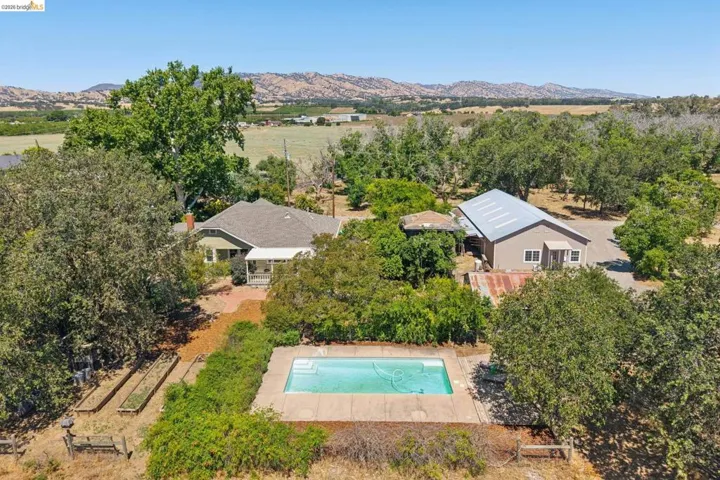 Expansive property featuring a rectangular swimming pool with concrete surround, a detached auxiliary structure with a metal roof, and a single-story residence with a covered porch