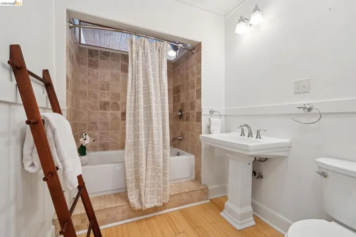 Pedestal sink with chrome fixtures, wainscoting, light wood-finish flooring, a white bathtub, and brown square tile surround