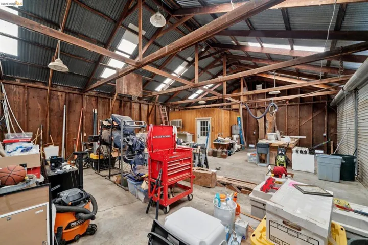 Spacious utility building featuring exposed wood beams, corrugated metal roofing, skylights, and a roll-up garage door