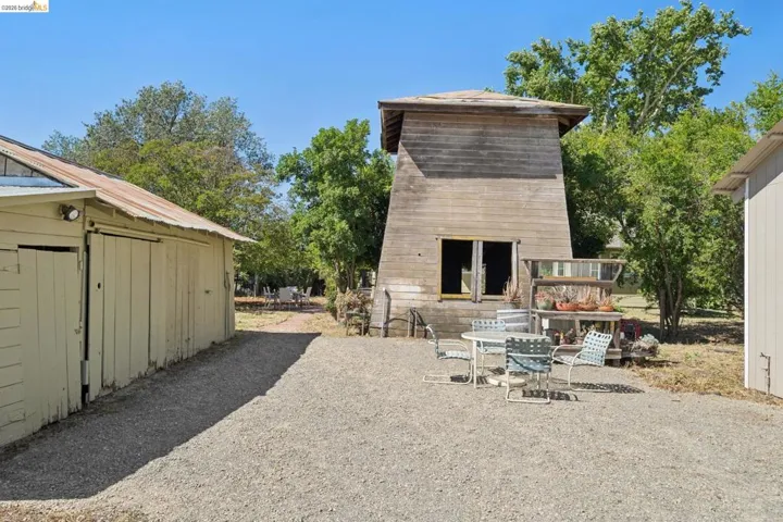 Gravel driveway with a wood-sided outbuilding, a second wood-sided structure, and a third building with vertical siding