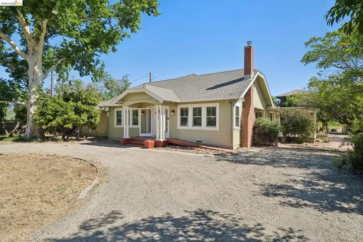 Traditional-style home featuring a light green exterior with white trim, a covered front porch with white columns, a red brick chimney, and a gravel driveway