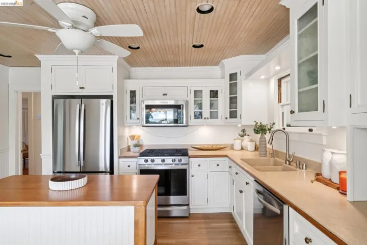 Kitchen featuring a wood-panel ceiling, white cabinetry, light countertops, stainless steel appliances, and a central island with a wood-finish top