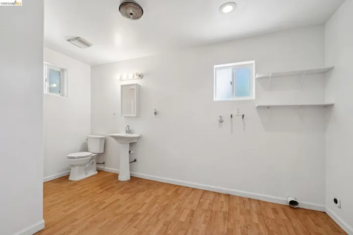 Spacious room featuring wood-finish flooring, a toilet, and a pedestal sink with a medicine cabinet