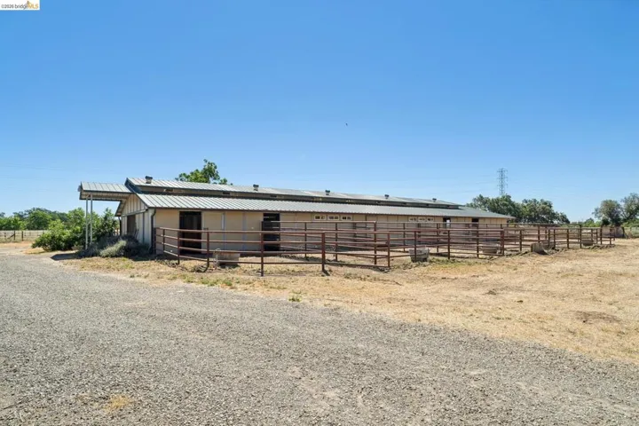 Agricultural structure with corrugated metal roofing, multiple stalls, attached covered overhang, and extensive metal paddock fencing