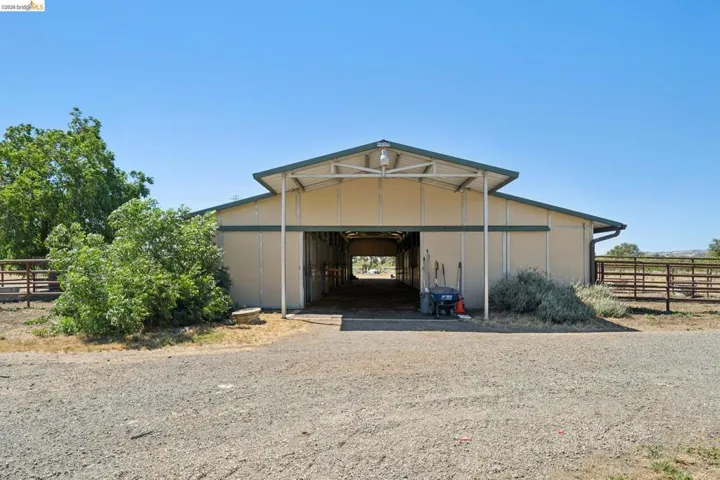 Expansive barn structure featuring a light-colored exterior, dark green trim, and a covered entry
