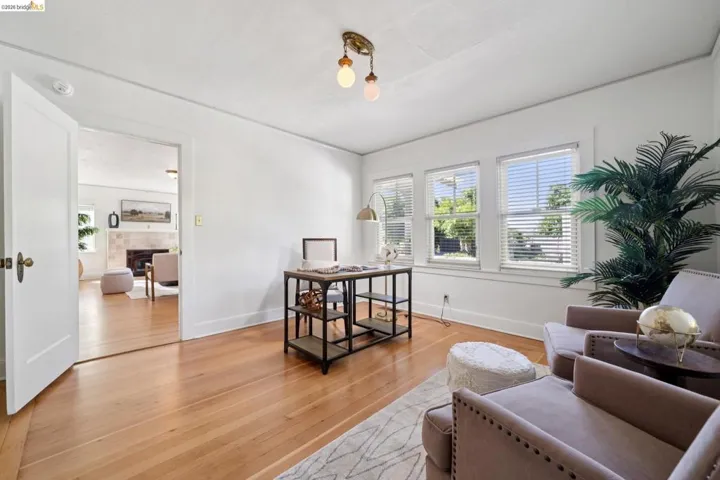 Bright room with hardwood flooring, white walls, multiple windows with blinds, and a brass-finish flush mount light fixture