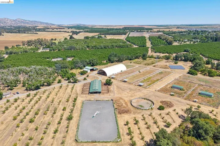 Expansive agricultural property featuring multiple cultivated fields, an outdoor riding arena, and an arched fabric structure