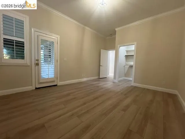 Spacious room featuring wood-finish flooring, crown molding, and neutral wall tones