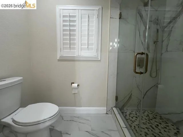 Shower enclosure with clear glass door, brass-finish hardware, and a pebble-stone floor
