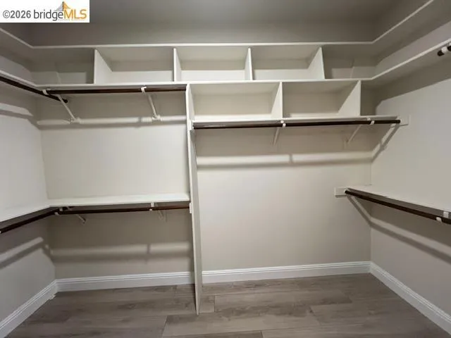 Custom closet system featuring wood-finish flooring, white shelving, multiple hanging rods, corner shelving, and crown molding