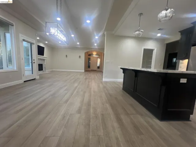 Spacious open-concept living area featuring wood-finish flooring, recessed lighting, and a contemporary linear chandelier
