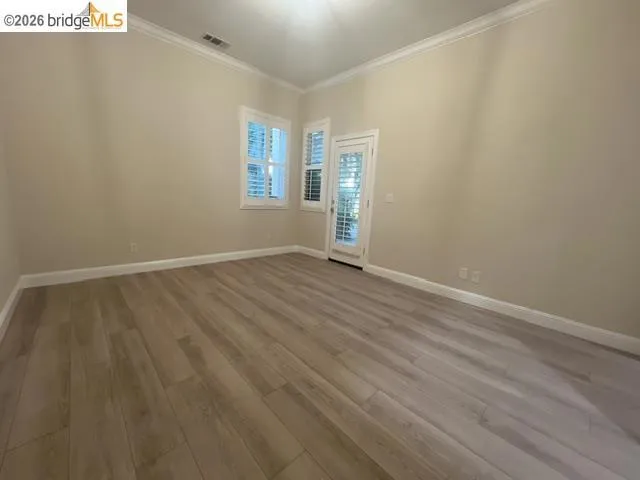 Spacious room featuring wood-finish flooring, neutral paint tones, crown molding, and white baseboards
