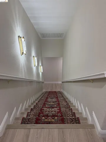 Staircase featuring wood-finish treads, a patterned runner, and white baseboards