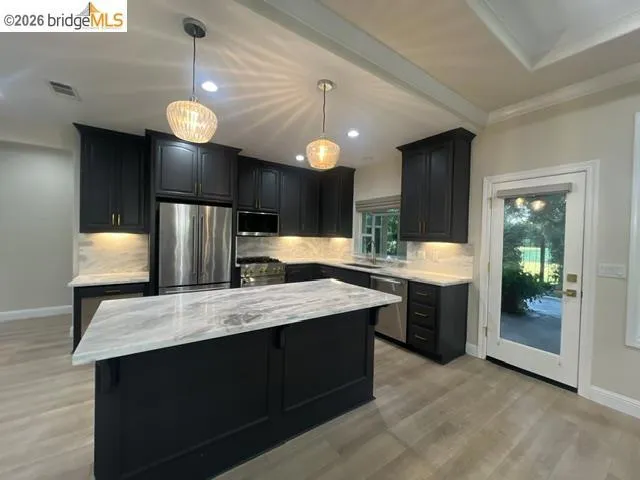 Modern kitchen featuring dark cabinetry with gold-tone hardware, stainless steel appliances, and light-toned, veined countertops