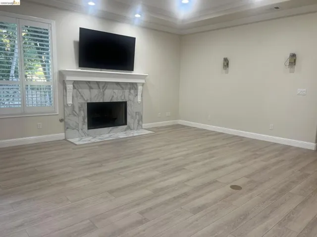 Spacious room featuring light wood-finish flooring, a contemporary fireplace with a marble-patterned surround, and white plantation shutters