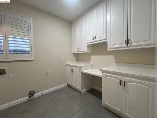 Spacious utility room featuring extensive white cabinetry, light-toned countertops, a dedicated workspace, and dark tile flooring