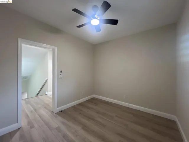 Neutral-toned room featuring light wood-finish flooring, white baseboards, and a ceiling fan with integrated lighting