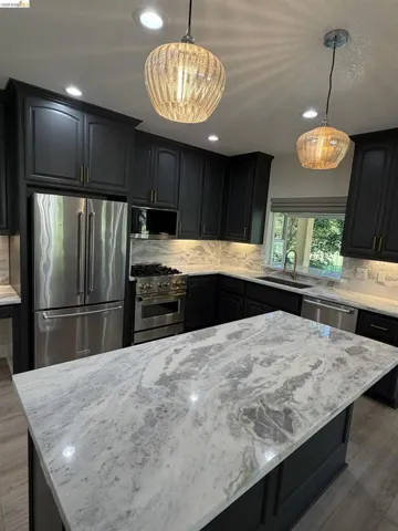 Kitchen island with a light-toned stone countertop, dark cabinetry, and integrated stainless steel appliances