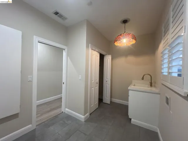 Laundry area featuring gray tile flooring, a white vanity with an integrated sink, a brushed gold-tone faucet, and white plantation shutters