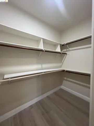 Walk-in closet featuring extensive built-in shelving, multiple hanging rods, and wood-finish flooring