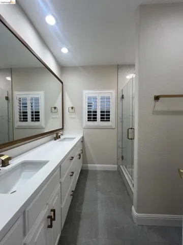 Bathroom featuring a dual vanity with white cabinetry, integrated sinks, and brass-finish hardware