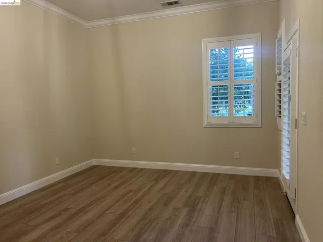 Gorgeous golf course view.  Spacious room featuring wood-finish flooring, neutral wall tones, elegant crown molding, and white window shutters