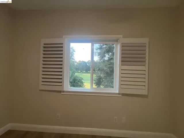 Gorgeous golf course view. Window with white plantation shutters providing a scenic backdrop of trees and an open field