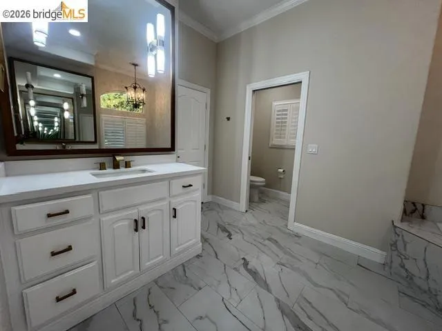 White vanity with quartz countertop, undermount sink, and brass-finish faucet