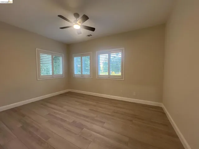 Gorgeous golf course view. Spacious room featuring wood-finish flooring, neutral-toned walls, and multiple windows with plantation shutters