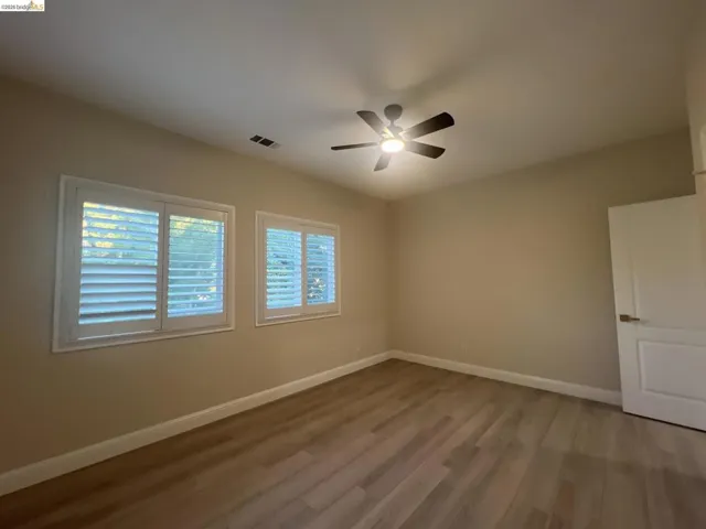 Upstairs. Gorgeous views of golf course.  Room featuring two windows with white plantation shutters, wood-finish flooring, a ceiling fan with integrated lighting, and a white paneled door with a brushed nickel handle
