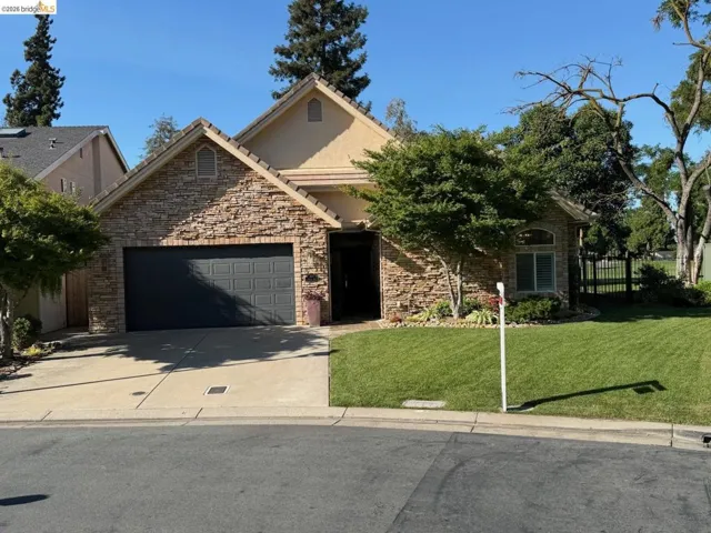 Stone-veneer facade with a dark garage door, arched entry, and mature landscaping