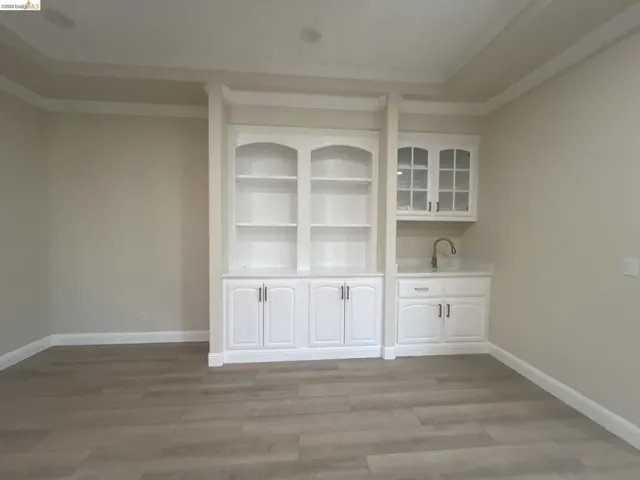 Built-in white cabinetry with open shelving, glass-front upper cabinets, and a wet bar featuring a single-basin sink