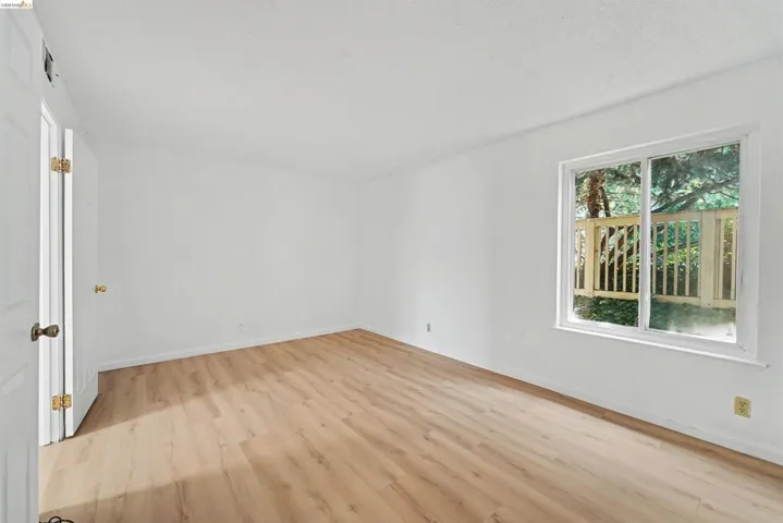 Spacious room with wood-finish flooring, white walls, and a large window