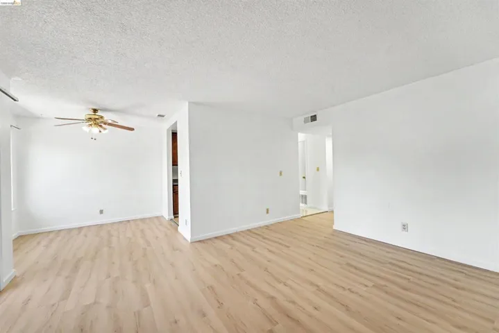 Spacious interior featuring light wood-finish flooring, white walls, and a ceiling fan with integrated lighting