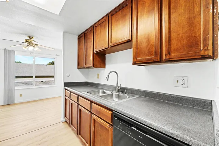 Kitchen area featuring wood cabinetry, a double basin stainless steel sink with a gooseneck faucet, gray countertops, and a black built-in dishwasher