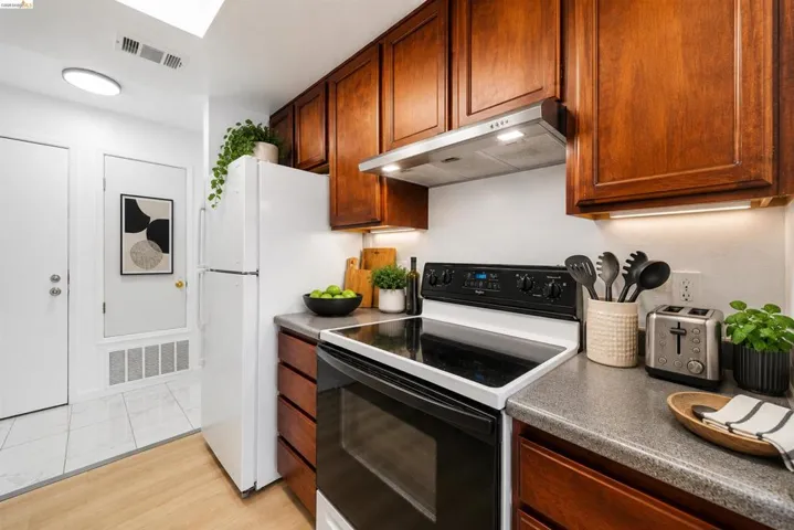 Well-appointed kitchen featuring wood-finish cabinetry, solid surface countertops, a white top-freezer refrigerator, and a black electric range with a stainless steel vent hood