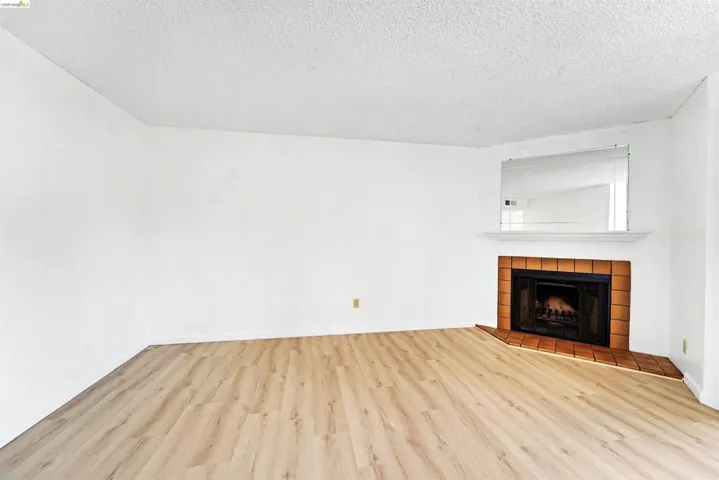 Living area featuring wood-finish flooring, a corner fireplace with a tile surround, a white mantel, and an integrated mirror
