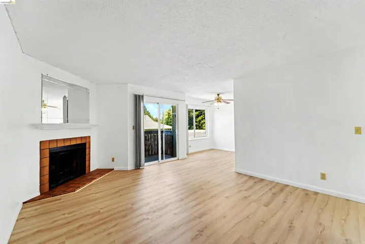 Spacious room featuring wood-finish flooring, a fireplace with a tile surround and hearth, white walls, and a sliding glass door to an exterior balcony